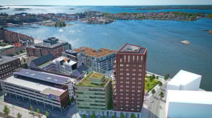 Flygbild över en stad vid vattnet med flera byggnader, inklusive ett höghus, parkeringshus och mindre bostadshus