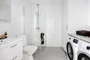 Modernt badrum med vit kakelvägg, dusch med glasvägg, tvättmaskin, toalett och handfat med spegelskåp