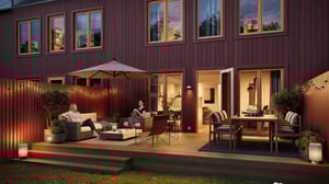 Radhus med träfasad och upplyst terrass. Två personer sitter på utomhusmöbler kring en eldstad, med matbord och parasoll i bakgrunden