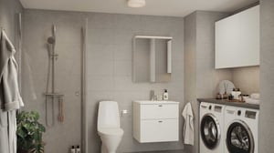 Modernt badrum med duschhörna, toalett, vit kommod med spegelskåp, tvättmaskin och torktumlare samt grå kakelväggar