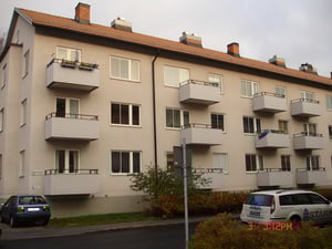 Flerfamiljshus med balkonger och tegeltak, parkerade bilar framför byggnaden