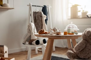 Barnrum med träbord, leksaker och en gunga formad som en elefant. Bakgrunden inkluderar klädhängare med barnkläder och mjuk belysning