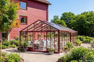 Personer som sitter vid ett bord i ett växthus utanför ett rött flerbostadshus