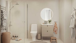 Modernt badrum med dusch med glasvägg, vit toalett, rund spegel ovanför ett skåp och olika badrumsartiklar