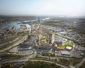 Luftbild av en stadsutvecklingsområde med byggnader, grönområden och vägar, omgiven av industriell infrastruktur och vatten