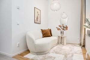 Modern vardagsrum med ljus soffa, bruna kuddar, sidobord med en vas och blommor, väggkonst, och hängande taklampor