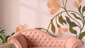 Rosa sammetssoffa framför en vägg med blommigt väggmotiv i pastellfärger