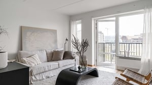 Ljusa vardagsrum med soffa, svart soffbord, balkongdörr och stora fönster