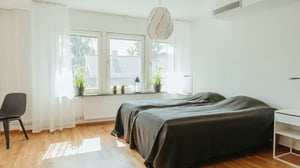 Lägenhet med två bäddar, ljusa väggar och stort fönster med gardiner