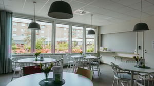 Tomt rum i modern gemensamhetslokal med runda bord, stolar och stora fönster