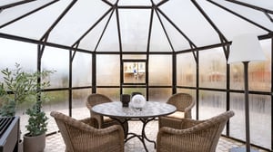 Inglasad uteplats med runt bord, fyra rottingstolar, växt och golvlampa