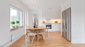 Inflyttningsklart kök och matplats i ljus öppen planlösning med träbord, stolar och rostfri kyl