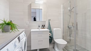 Modernt badrum med tvättmaskin, kommod, toalett och duschhörna