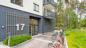 Flerbostadshus med nummer 17, entré och cykelparkering vid grönskande skogsmiljö