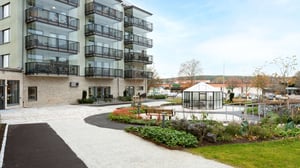 Flerfamiljshus med balkonger och innergård med planteringar, gångvägar och sittbänk