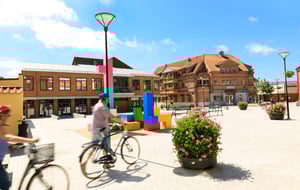 Torg med cyklister, blommande planteringar och röda tegelhus under en blå himmel