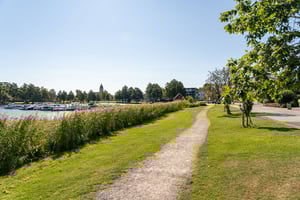 Promenadväg i Strängnäs längs vattnet med grön park, båtar och träd under klar himmel