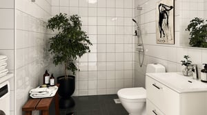 Badrum med vita kakelväggar, mörkt golv, dusch, toalett, handfat och grön växt