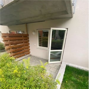 Uteplats under balkong, stenlagt golv och gröna buskar