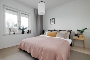 Sovrum med dubbelsäng, ljusa väggar och fönster med växter på fönsterbrädan