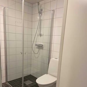 Inflyttningsklart badrum med duschhörna, vita kakelväggar och toalett
