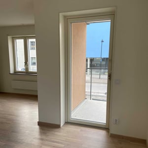 Inflyttningsklar lägenhet med ljusa väggar, trägolv, fönster och glasdörr mot balkong