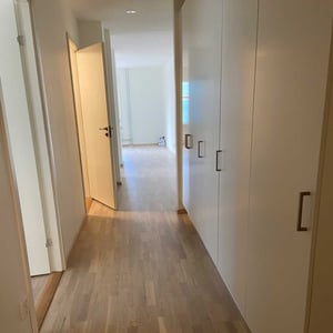 Rum i ljus korridor med trägolv och vita garderober