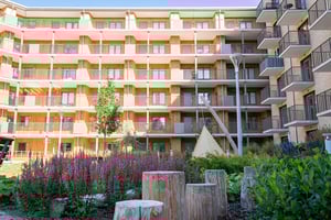 Flerfamiljshus med balkonger och grön innergård med blommor och träpallar