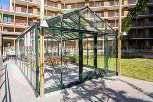 Glasat uterum med bord på  en innergård, omgiven av flerfamiljshus