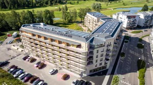 Modernt flerbostadshus med balkonger, parkeringsyta och grönområden i bakgrunden