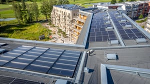 Flygvy över bostadshus med solpaneler på taket, gröna omgivningar och en byggnad med balkonger