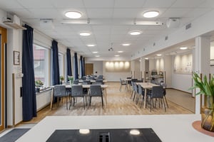 Tomt rum med ljusa bord och grå stolar i en modern lokal med trägolv och stora fönster