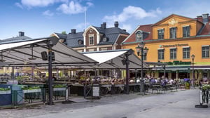 Uteservering på ett torg med människor och färgglada byggnader i bakgrunden