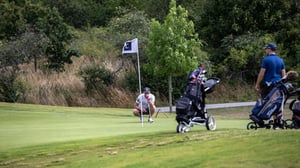 Golfspelare i vitt som puttar vid flaggan på en golfbana, med två golfvagnar i förgrunden