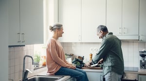 Två personer i ett ljust kök, där en man skär grönsaker vid köksbänken
