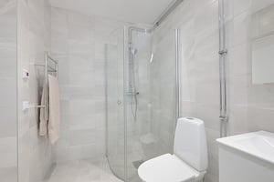Modernt vitt badrum med dusch bakom glasvägg, toalett och handdukstork