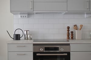 Modernt kök med vita kakelväggar, grå skåpsluckor och inbyggd ugn