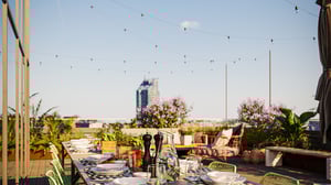 Uteservering med dukat bord, växter och utsikt mot stadens skyline under klar himmel