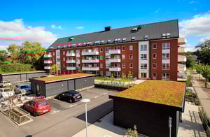 Flerbostadshus i rött tegel med balkonger och parkeringsplats framför under blå himmel