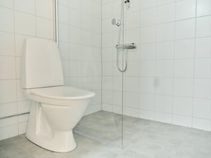 Badrum med toalett, duschhörna och vita kakelväggar