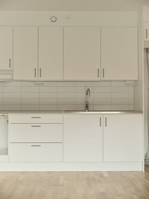 Inflyttningsklart kök med vita skåp, kaklad vägg och trägolv