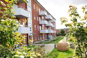 Rött flerbostadshus med balkonger och grön innergård