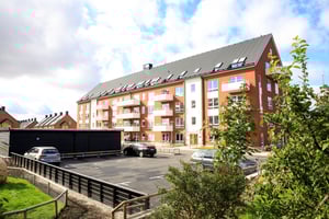 Rött flerfamiljshus med balkonger och parkeringsplats utanför