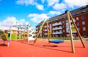 Lekplats med gungställning och klätterlek framför ett flerbostadshus