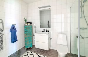 Modernt badrum med vita kaklade väggar, duschhörna, toalett och handfat med spegel