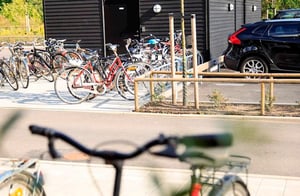Cykelparkering vid ett svart flerbostadshus med flera parkerade cyklar och en bil