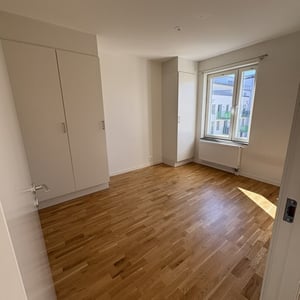 Inflyttningsklar lägenhet med tomt rum, trägolv, vita garderober och fönster med radiator under