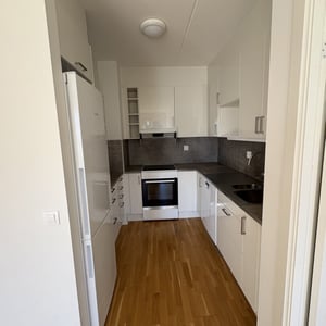 Inflyttningsklar lägenhet med kompakt kök, vita skåp, mörk bänkskiva och trägolv