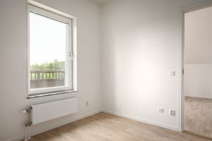 Inflyttningsklar lägenhet med ljusa väggar, trägolv, fönster och radiator