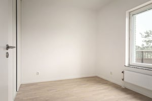 Inflyttningsklart rum med ljusa väggar, trägolv och fönster mot balkong